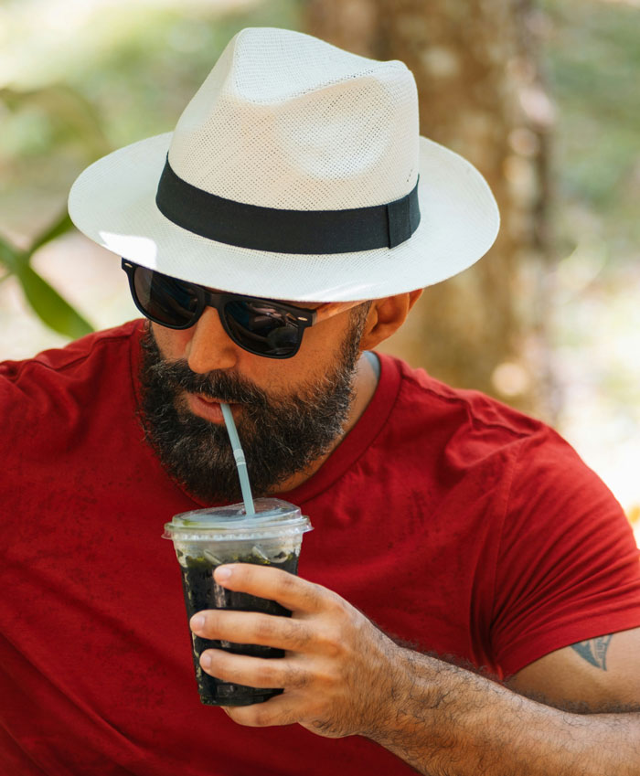 A man with a beard and hat sips a drink through a straw, engaged in a casual conversation, possibly about women not being wife material.