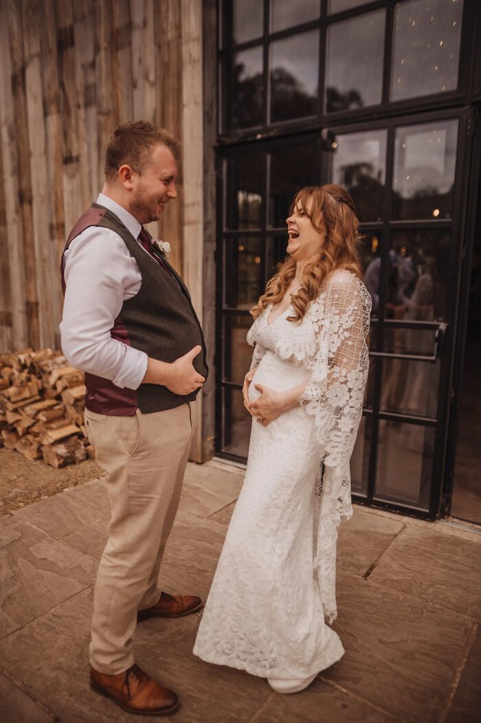 A bride and groom sharing a laugh, making a funny wedding photo outside a rustic venue.