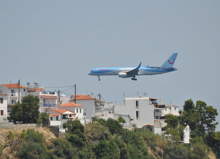 A blue plane's jet engine flies low over white buildings, posing a risk of severe injuries.