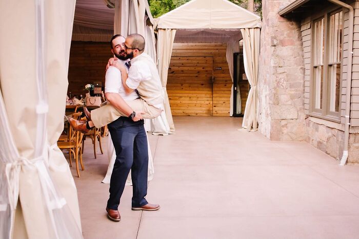 Funny wedding photos: Groom carrying his husband, sharing a kiss, in a playful and iconic moment.