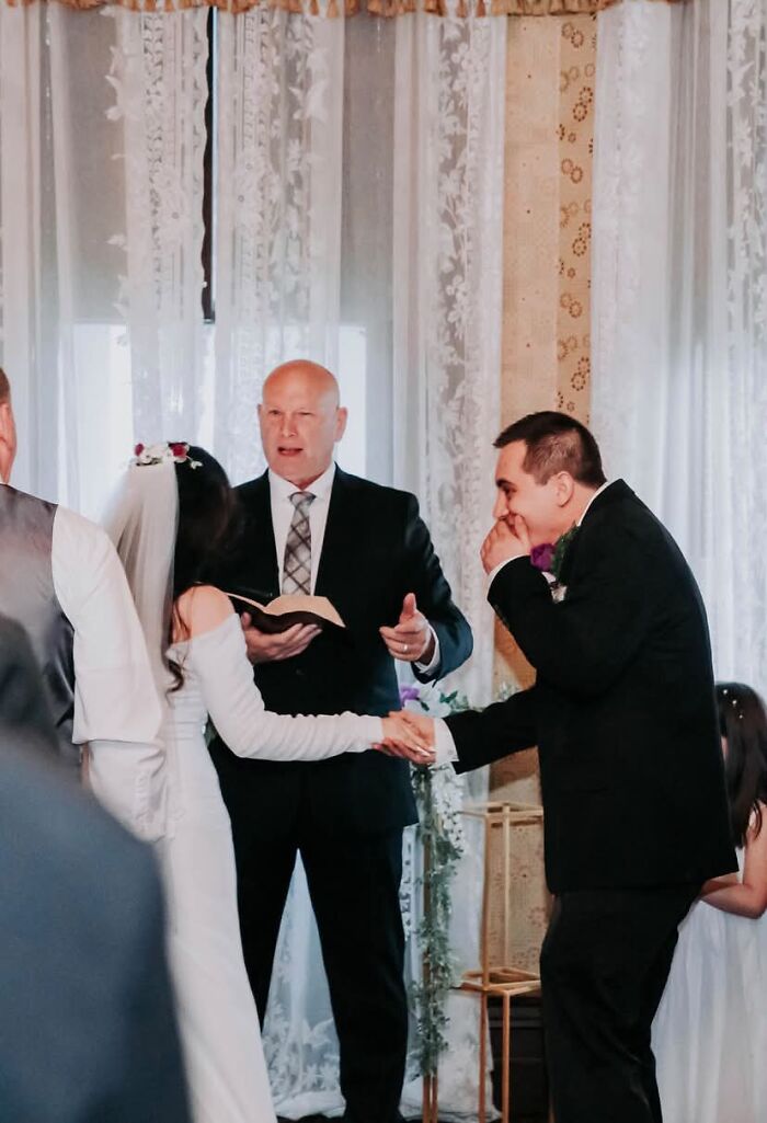 Funny wedding photos: Groom laughing and wiping tears while holding hands with the bride during the ceremony.