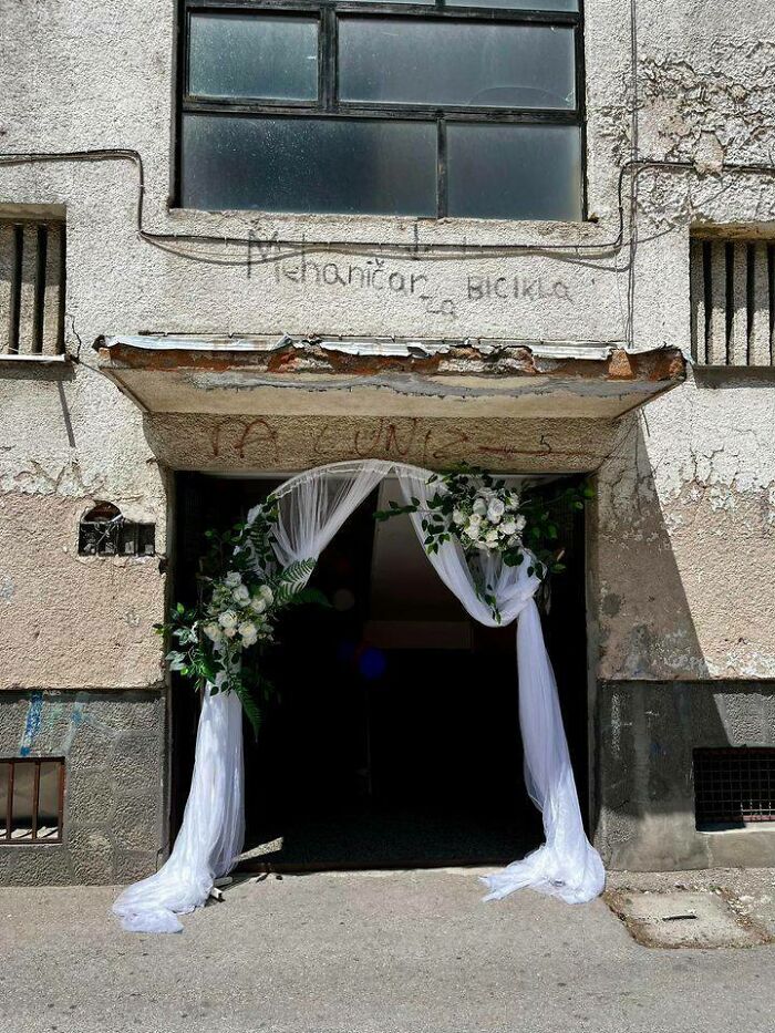 An ornate white floral archway at the entrance of a dilapidated building, highlighting Eastern European contrasts.