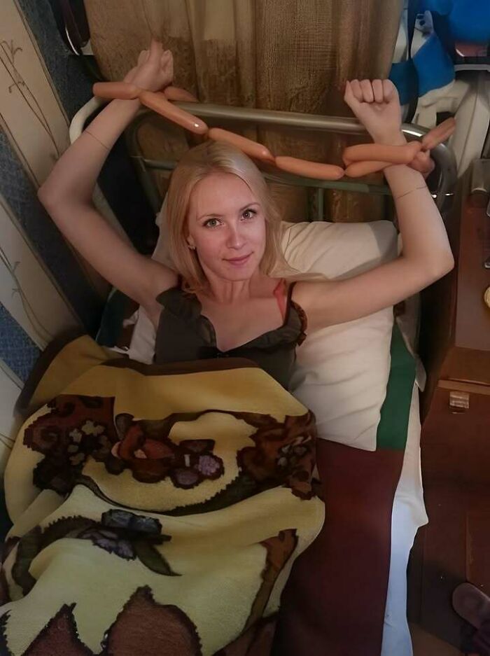 A woman in bed with her wrists tied with a string of sausages, demonstrating how people from Eastern Europe are built different.