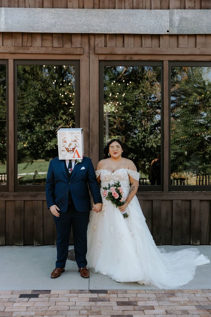 A funny wedding photo of a bride holding flowers next to a groom with a box on his head, creating an iconic wedding moment.