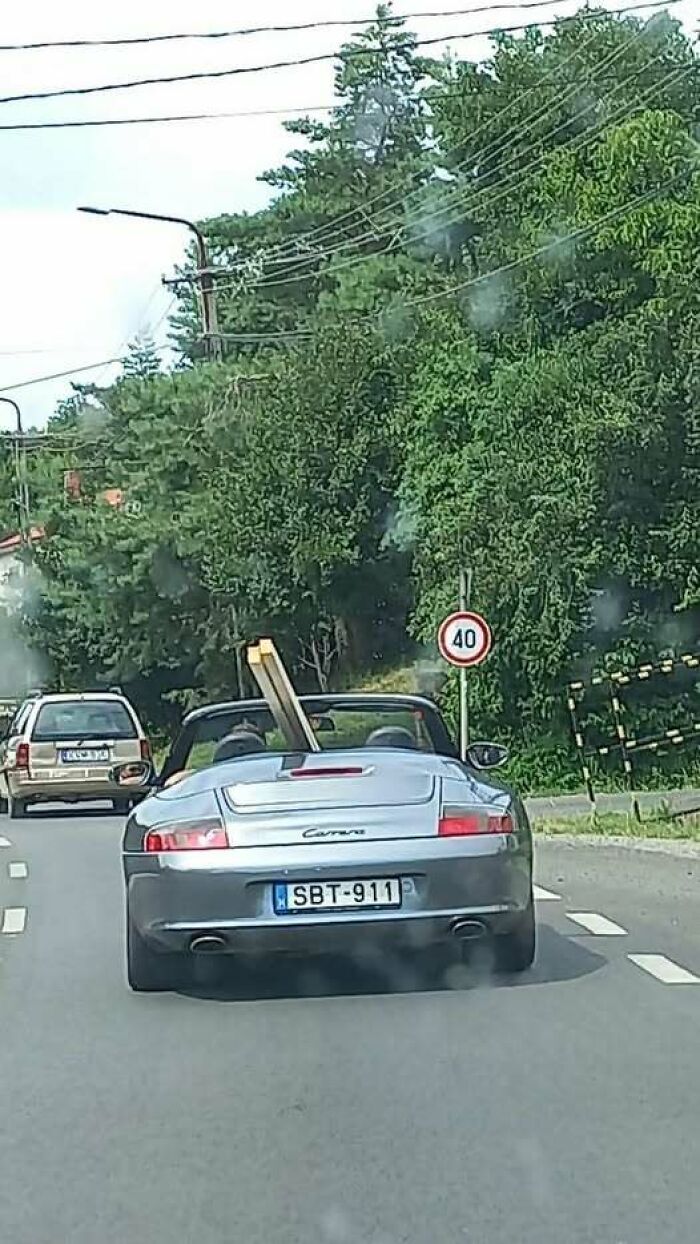 A convertible car from Eastern Europe carrying a large wooden plank, showing people built different.