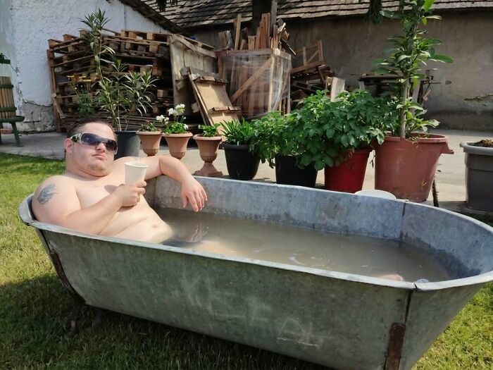 A man from Eastern Europe relaxing in an outdoor bathtub, a funny meme showing people built different.
