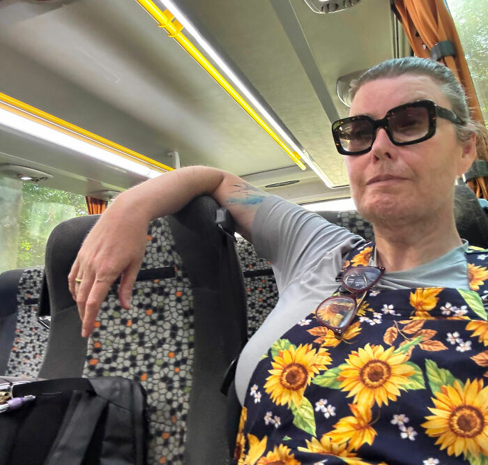 Trans American seated on a bus, wearing large sunglasses and a floral top, recounting horrors of European asylum center. Trans American seated on a bus, wearing large sunglasses and a floral top, recounting horrors of European asylum center.