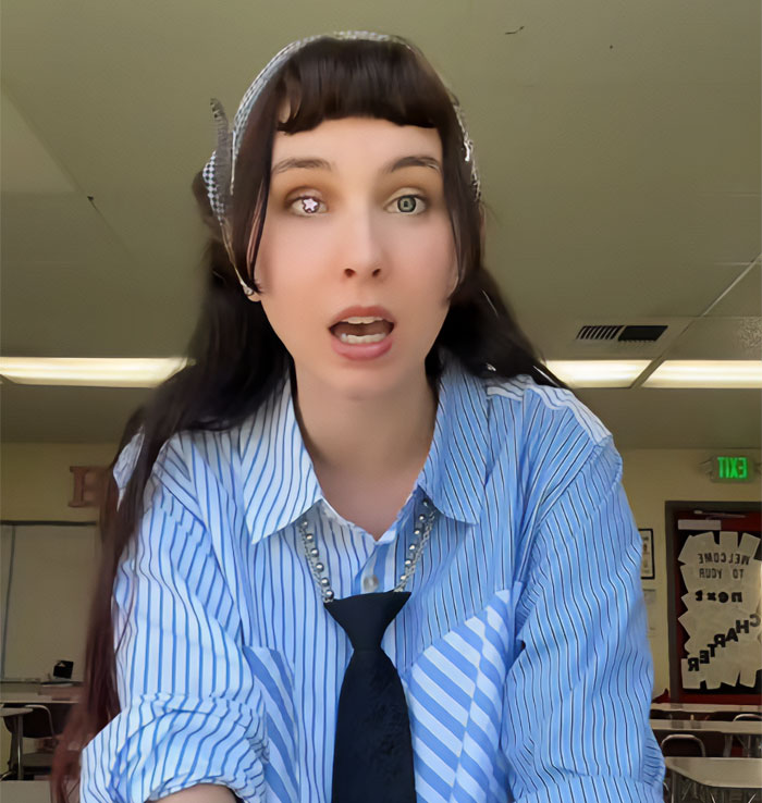 A teacher's OOTD selfie in a classroom, showing a woman with two different colored contact lenses and bangs, wearing a striped shirt and a black tie. A teacher's OOTD selfie in a classroom, showing a woman with two different colored contact lenses and bangs, wearing a striped shirt and a black tie.