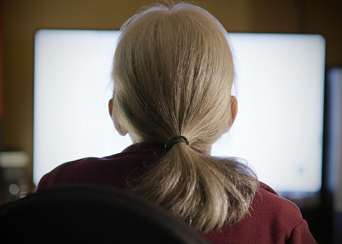 An old woman, back to camera, looking at a bright screen, affected by eBay's actions.