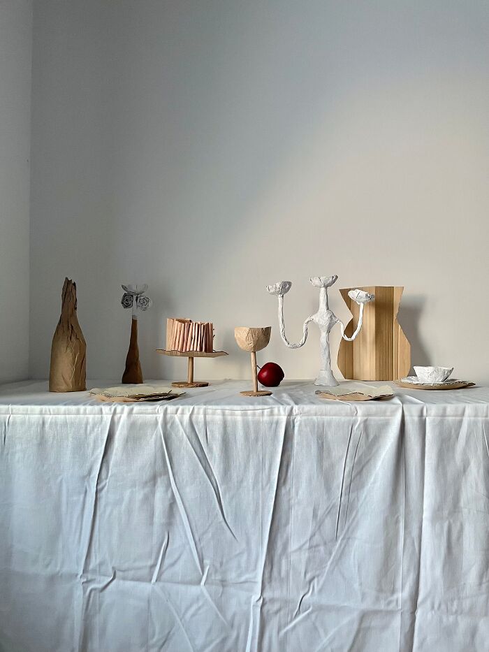 Table set with various surreal paper creations, including a bottle, candelabras, and plates, as art.