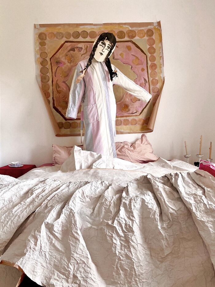 A figure made of surreal paper creations, wearing a paper coat and mask, standing on a bed of crumpled paper, blurring sculpture and fashion.
