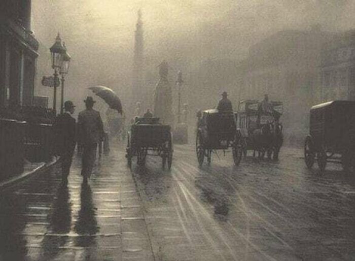 A foggy street scene with horse-drawn carriages and people walking with umbrellas, a moment nearly lost to history.