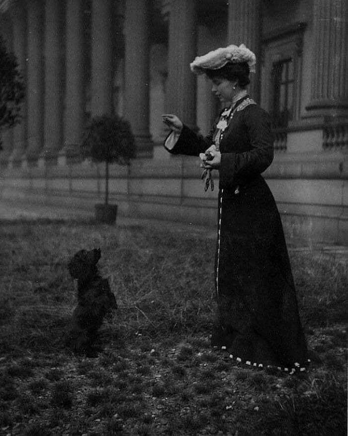 A black and white photo of a woman in a long dress training a dog, a moment from history.