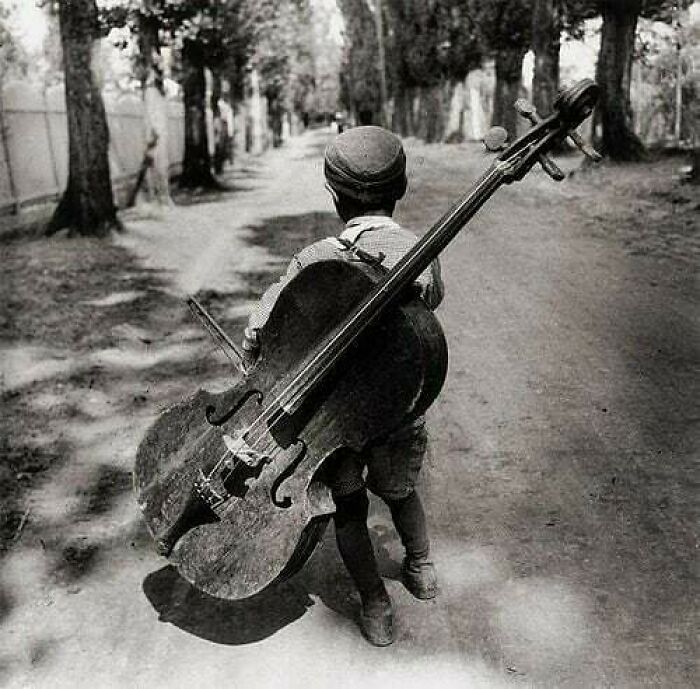 A young boy carries an oversized cello down a tree-lined path, a moment nearly lost to history.