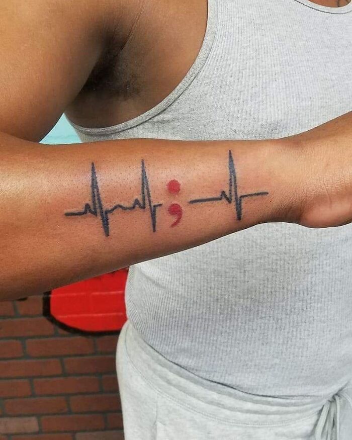 A man's forearm displaying a semicolon tattoo within a heartbeat line, illustrating a powerful story.