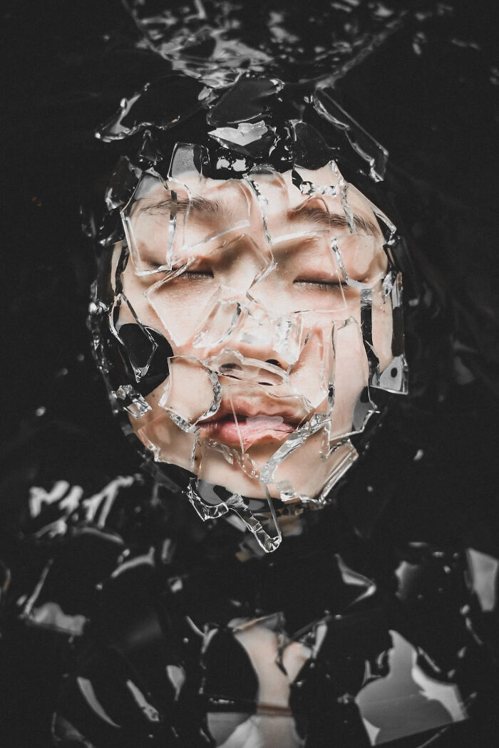An artistic close-up of a person's face covered in shattered glass, conveying abstract beauty. A winning image from the 2026 European Photography Awards.