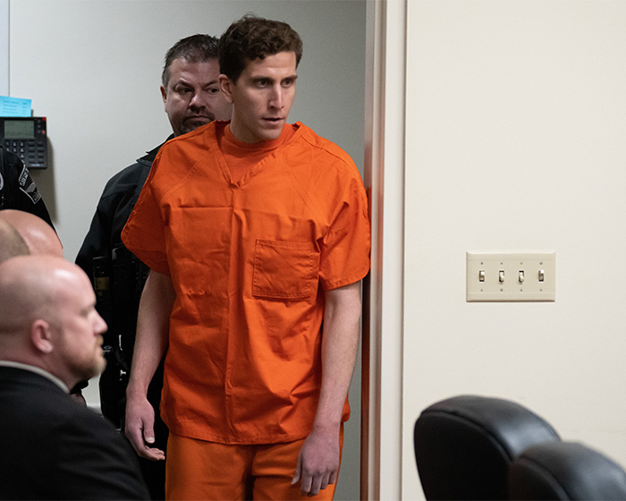 Bryan Kohberger in an orange jumpsuit, guarded by an officer, walks into a room. Netflix documentary on Bryan Kohberger's case.