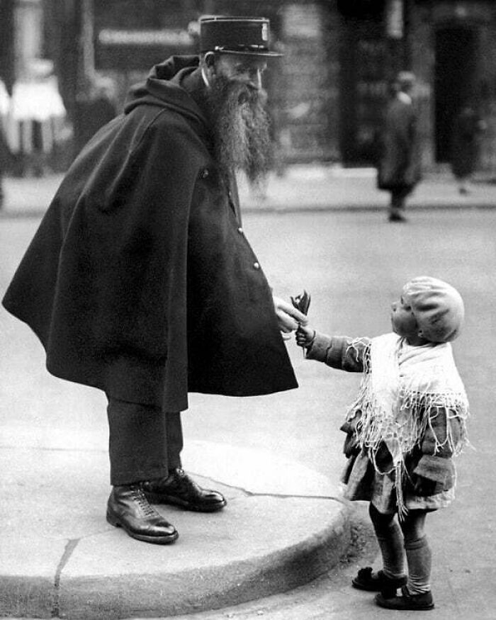 A little girl gives a flower to a tall, bearded policeman in a historic black and white photo, moments lost to history.
