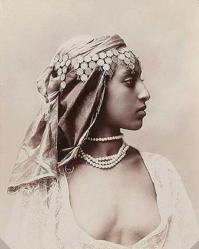 A sepia-toned profile of a woman with an ornate headpiece and pearl necklaces, a moment from history.
