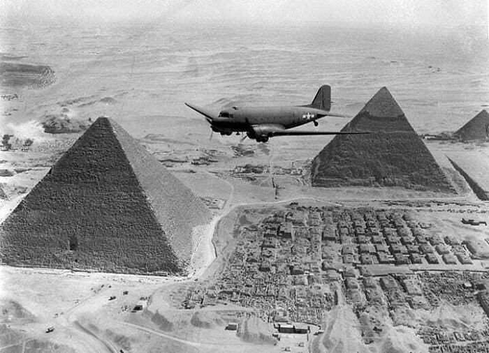 An old black and white photo of a military plane flying over the great pyramids, capturing a historical moment.