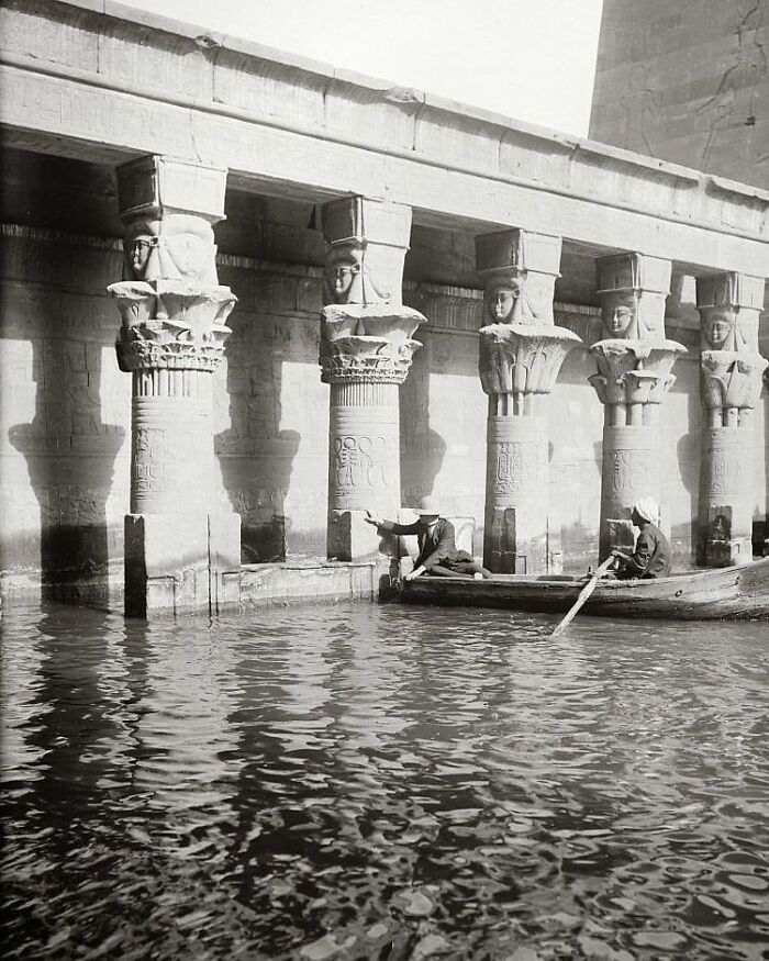Black and white photo of people in a boat on a river by an ancient Egyptian temple, moments lost to history.