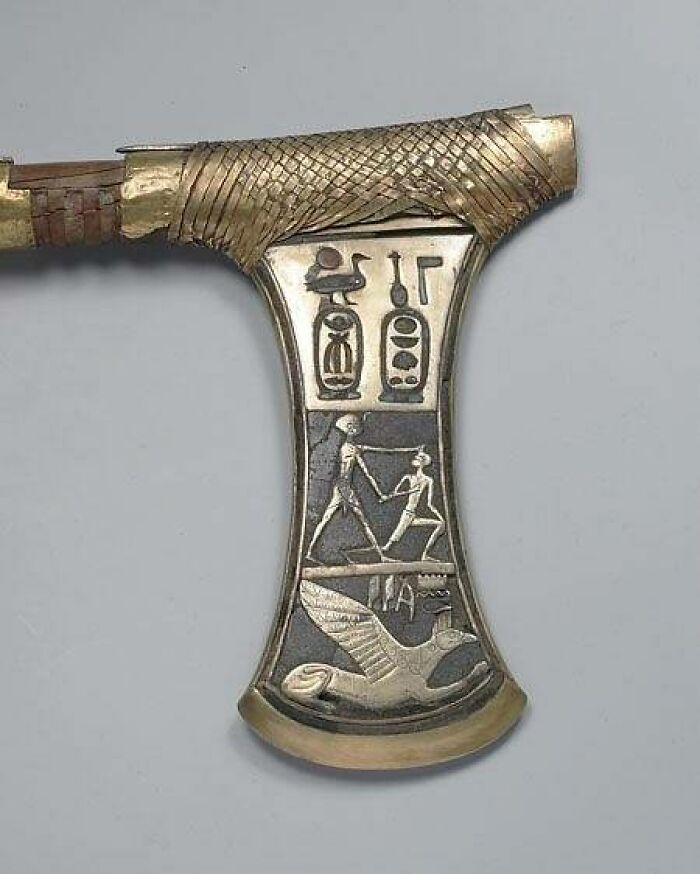 Close-up of an ancient Egyptian ceremonial axe with intricate gold and silver details, depicting historical moments.