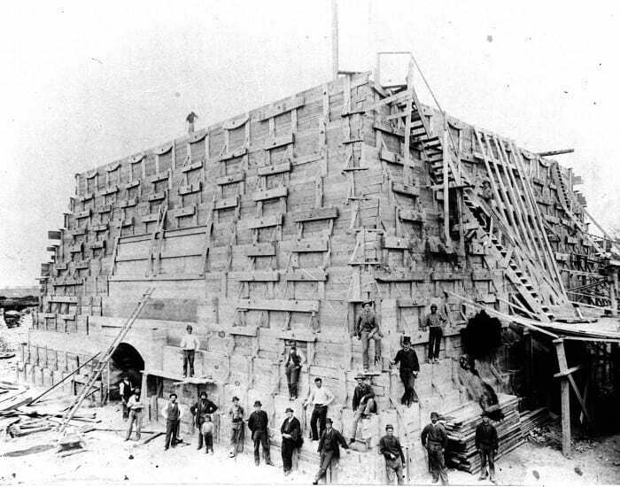 A group of workers stand on and around a massive, intricately shored wooden structure, a construction moment nearly lost to history.