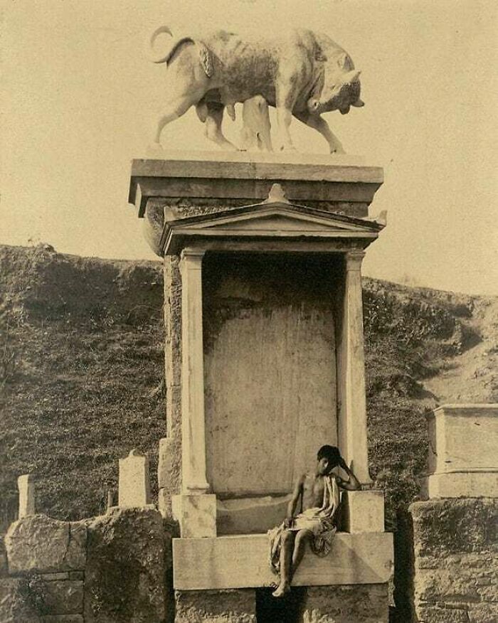 A man in traditional attire sitting by an ancient statue of a bull, showcasing a moment nearly lost to history.
