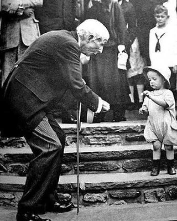 Elderly man leaning on a cane interacting with a small child on steps, a moment nearly lost to history.