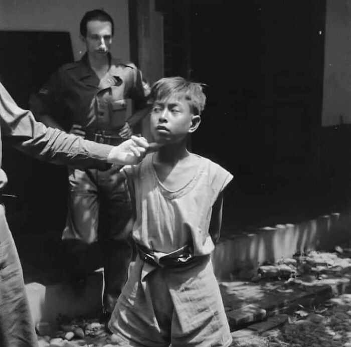 A solemn young boy is observed by two men in uniform, one reaching towards him, captured in a significant moment nearly lost to history.