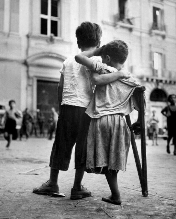 Two young boys, one with crutches, standing together in a street, capturing moments nearly lost to history.