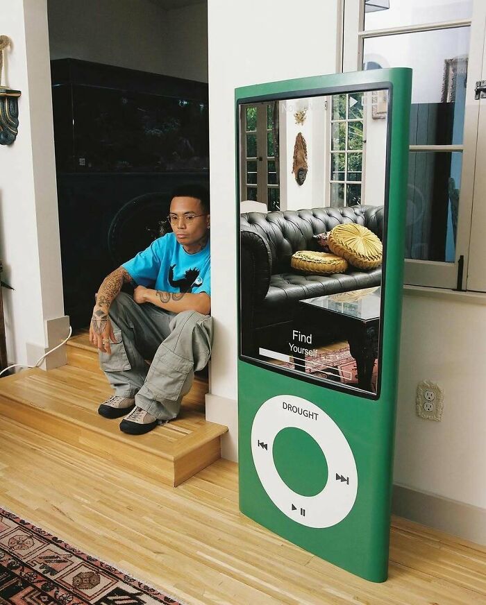 Brilliant and beautiful designs: A man sitting beside a large, green iPod-shaped mirror reflecting an interior, showcasing brilliant design.