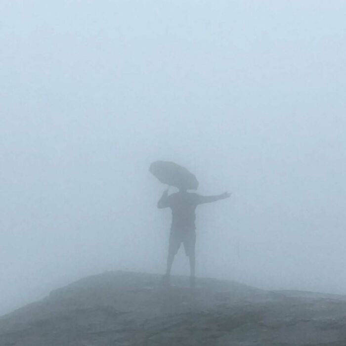 A person with an umbrella on a very foggy mountain, showing a trip that didnt go as planned.