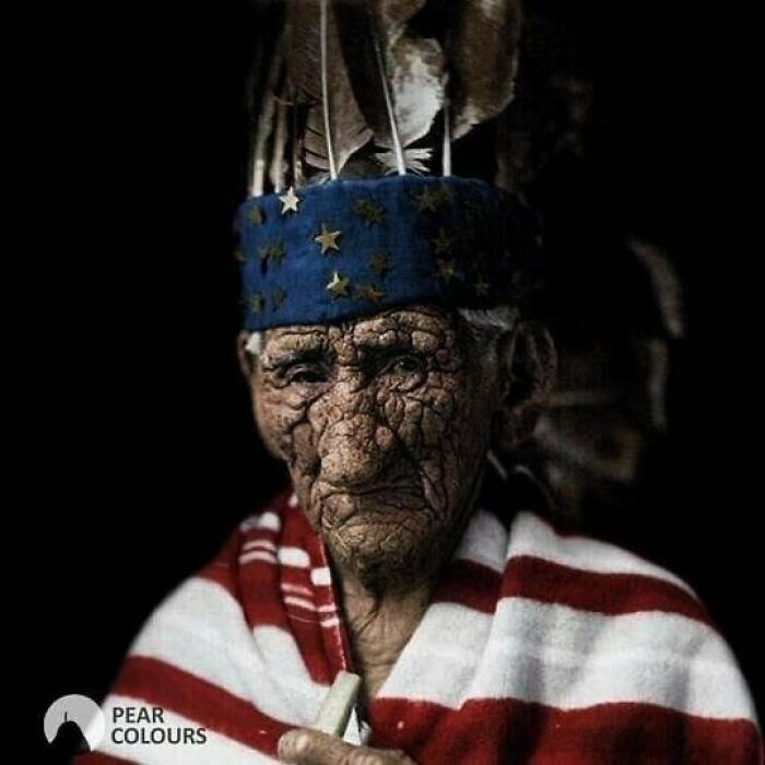 An elderly person with deeply wrinkled skin wears a blue hat with gold stars and feathers, wrapped in an American flag, showcasing moments nearly lost to history.
