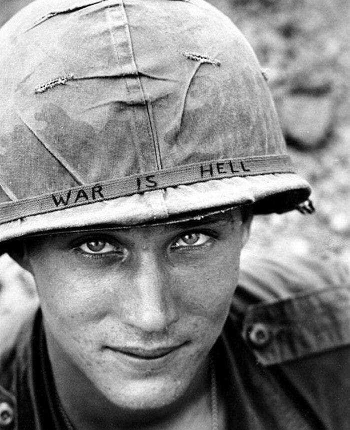 A close-up of a soldier with a helmet inscribed WAR IS HELL, capturing a poignant moment nearly lost to history.