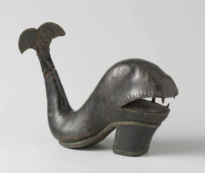 A detailed photo of a dark, whale-shaped leather shoe with teeth and a tail, an unusual moment nearly lost to history.