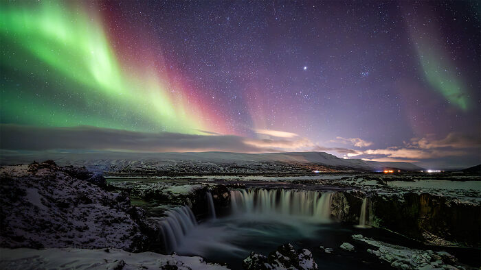 Mesmerizing astronomy photo of the Northern Lights over a waterfall in a snowy landscape, showcasing the universe.