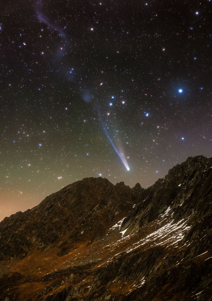 A bright comet with a tail streaks across a star-filled night sky above jagged mountains in an astronomy photo from the ZWO Shortlist.