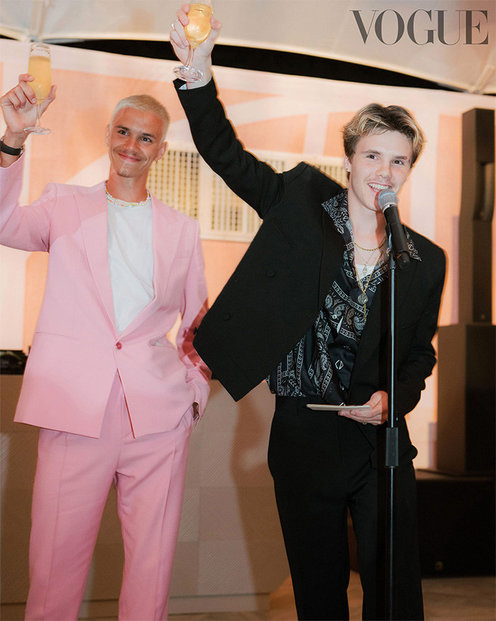 Two men raising glasses at a wedding reception, one in a pink suit and the other in a black suit with a microphone. Two men raising glasses at a wedding reception, one in a pink suit and the other in a black suit with a microphone.