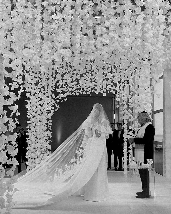 A black and white image of Nicola Peltz Beckham walking down the aisle, adorned with a long veil, at her wedding. A black and white image of Nicola Peltz Beckham walking down the aisle, adorned with a long veil, at her wedding.