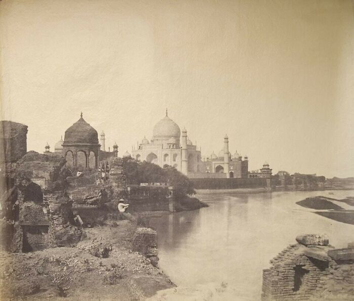 An old sepia photograph showing the Taj Mahal in the distance, with a river and crumbling structures in the foreground, a moment nearly lost to history.