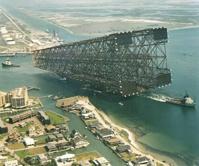 An enormous offshore platform being towed through a narrow waterway, moments lost to history.