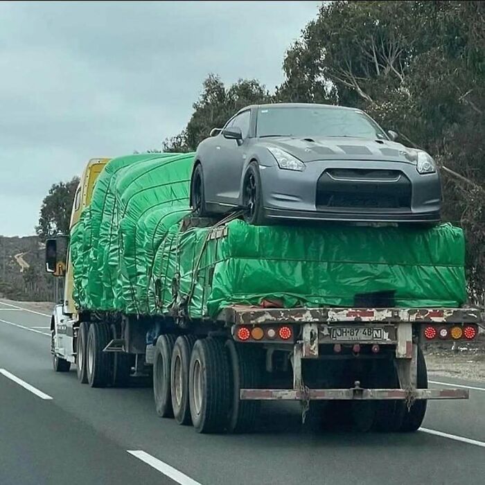 Funny car meme of a Nissan GT-R on top of a truck, covered in a green tarp, showing a unique way of transporting cars.