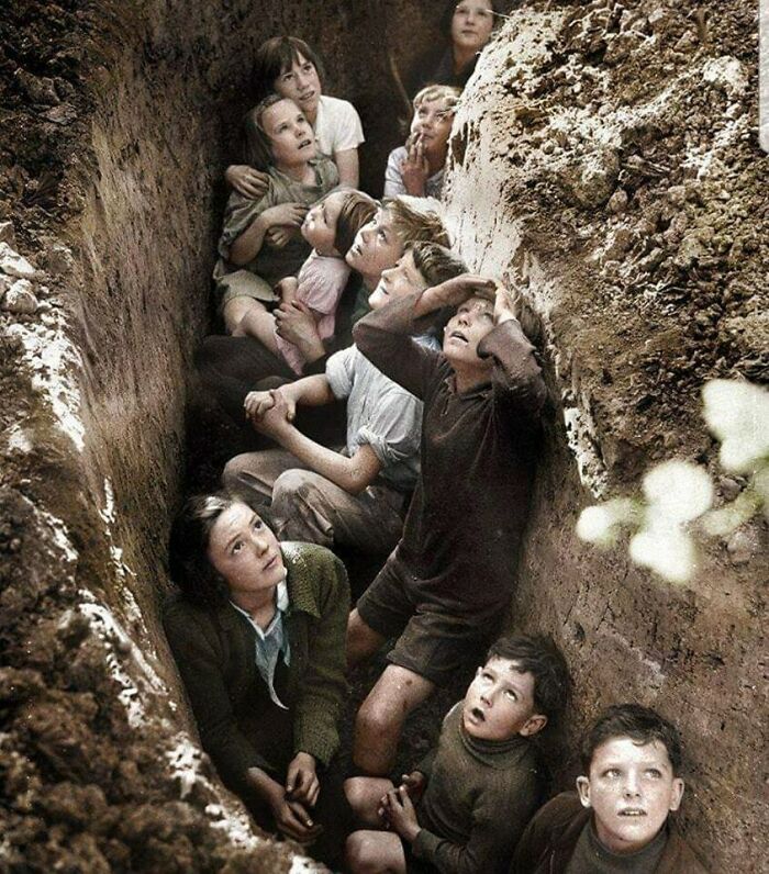 Children huddled in a trench, looking up at the sky, a poignant moment lost to history.