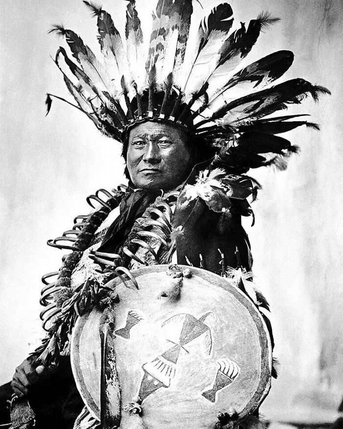 A Native American man in a feathered headdress holds a decorated shield, representing moments nearly lost to history.