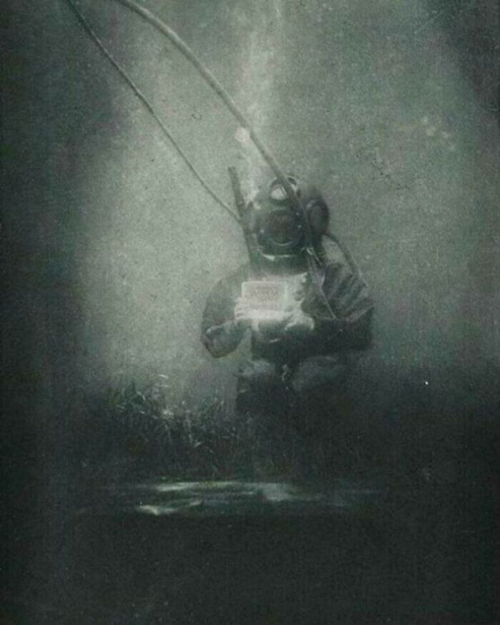 An old photograph of a deep-sea diver in a heavy suit and helmet, holding a bright object underwater, a moment nearly lost to history.
