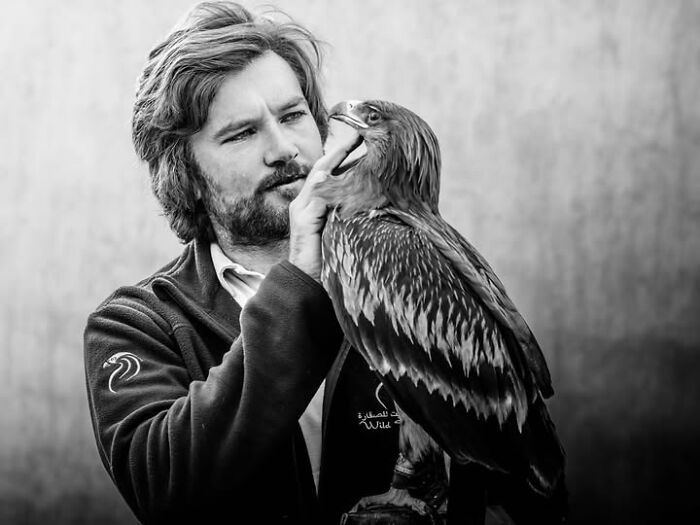 Remarkable photographs by Tittu Shaji Thomas capturing life: a man in black and white holding a large bird.
