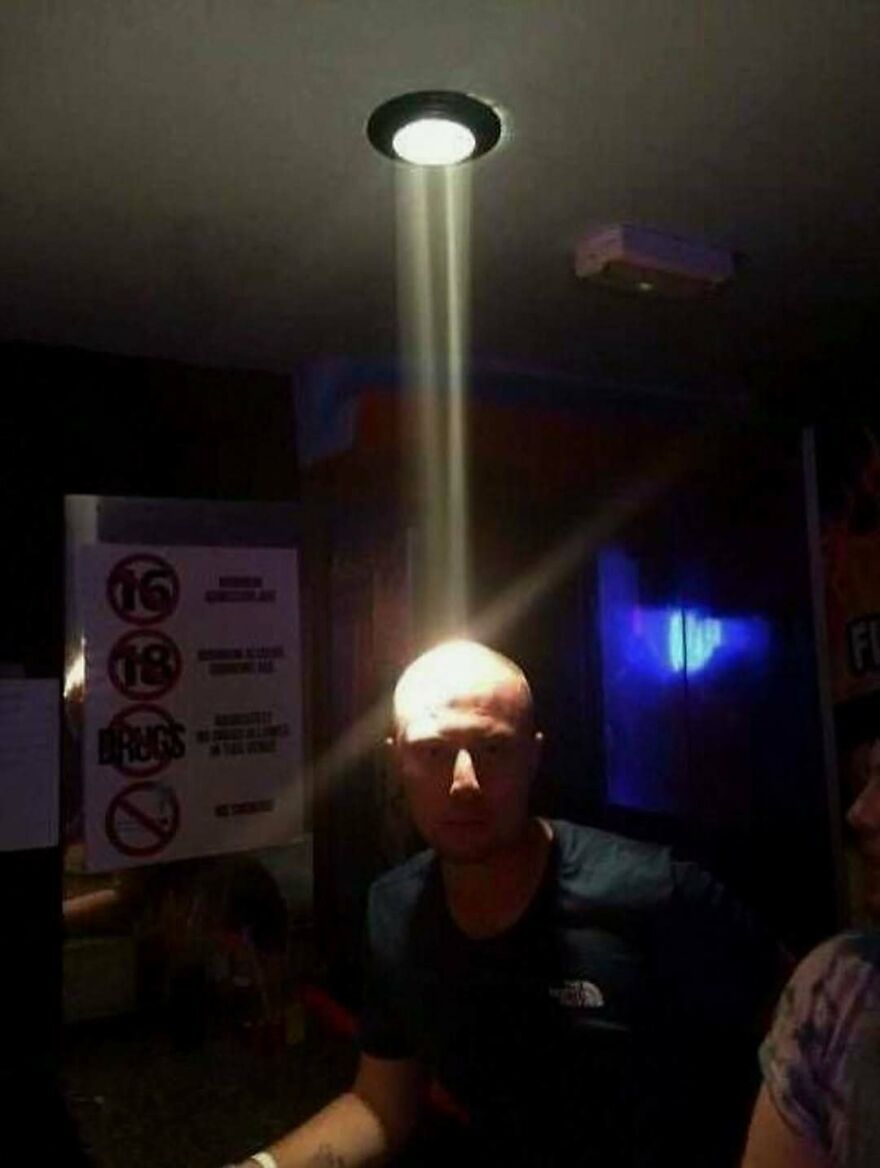 A man with a light beam shining directly on his head from a ceiling light, a random and unhinged image.