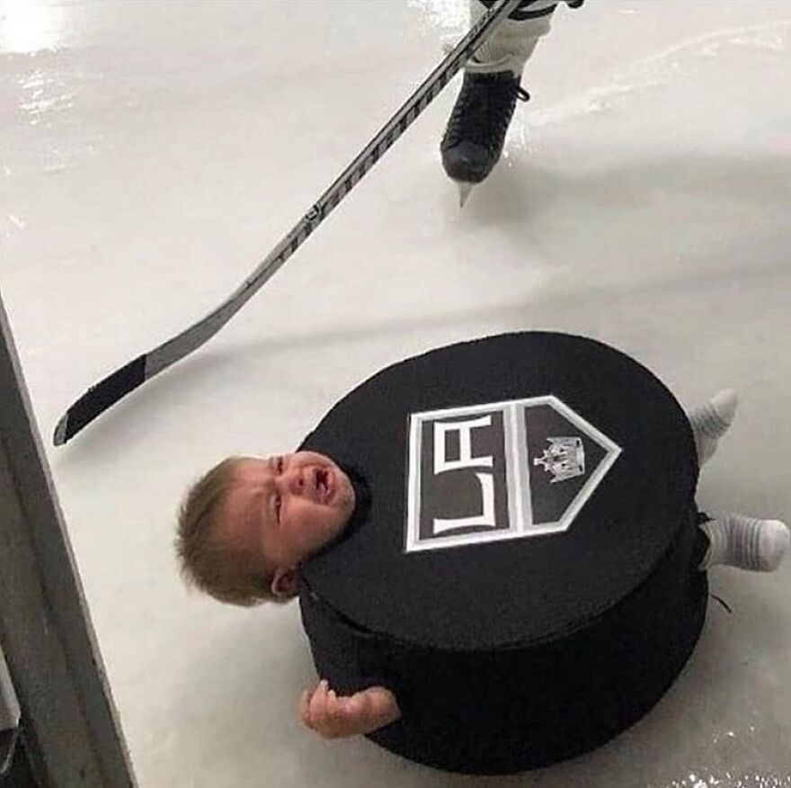 A cursed image of a baby in a hockey puck costume crying on the ice next to a hockey stick and skate.