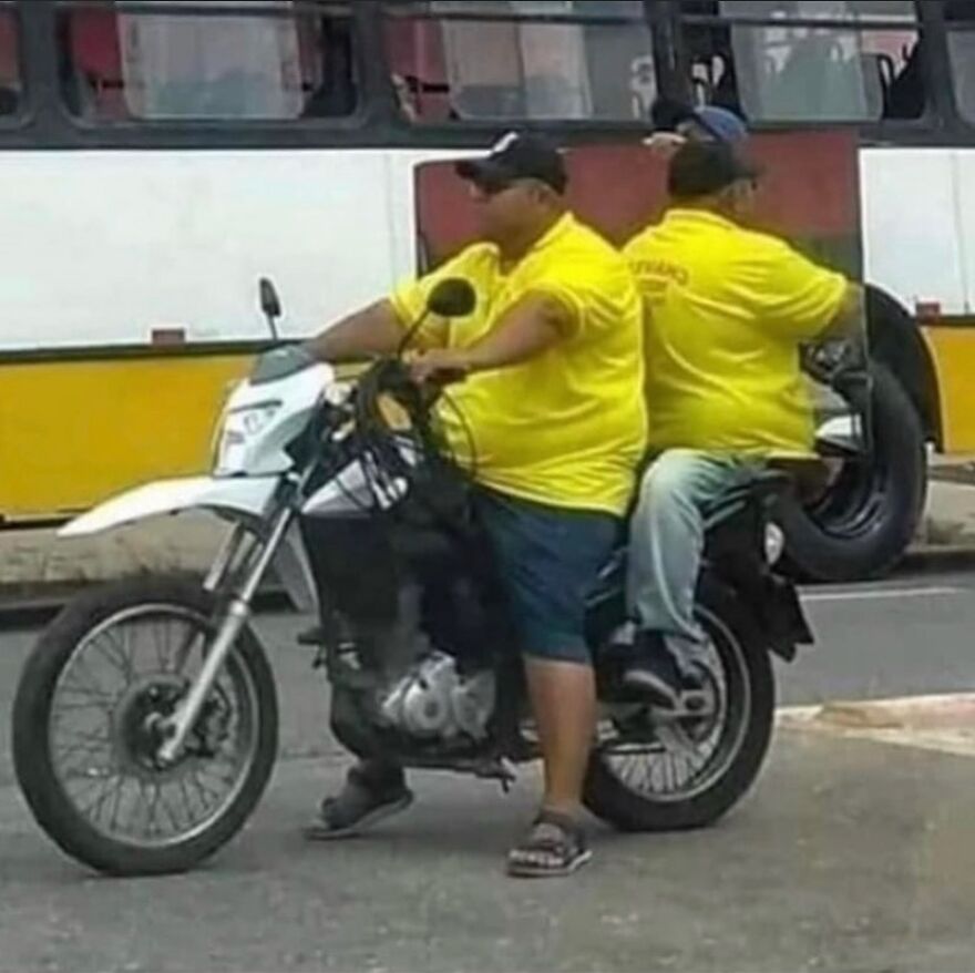 Two men in yellow shirts, sitting on a single motorcycle, with one looking like he is sitting on another man's lap, a cursed image.
